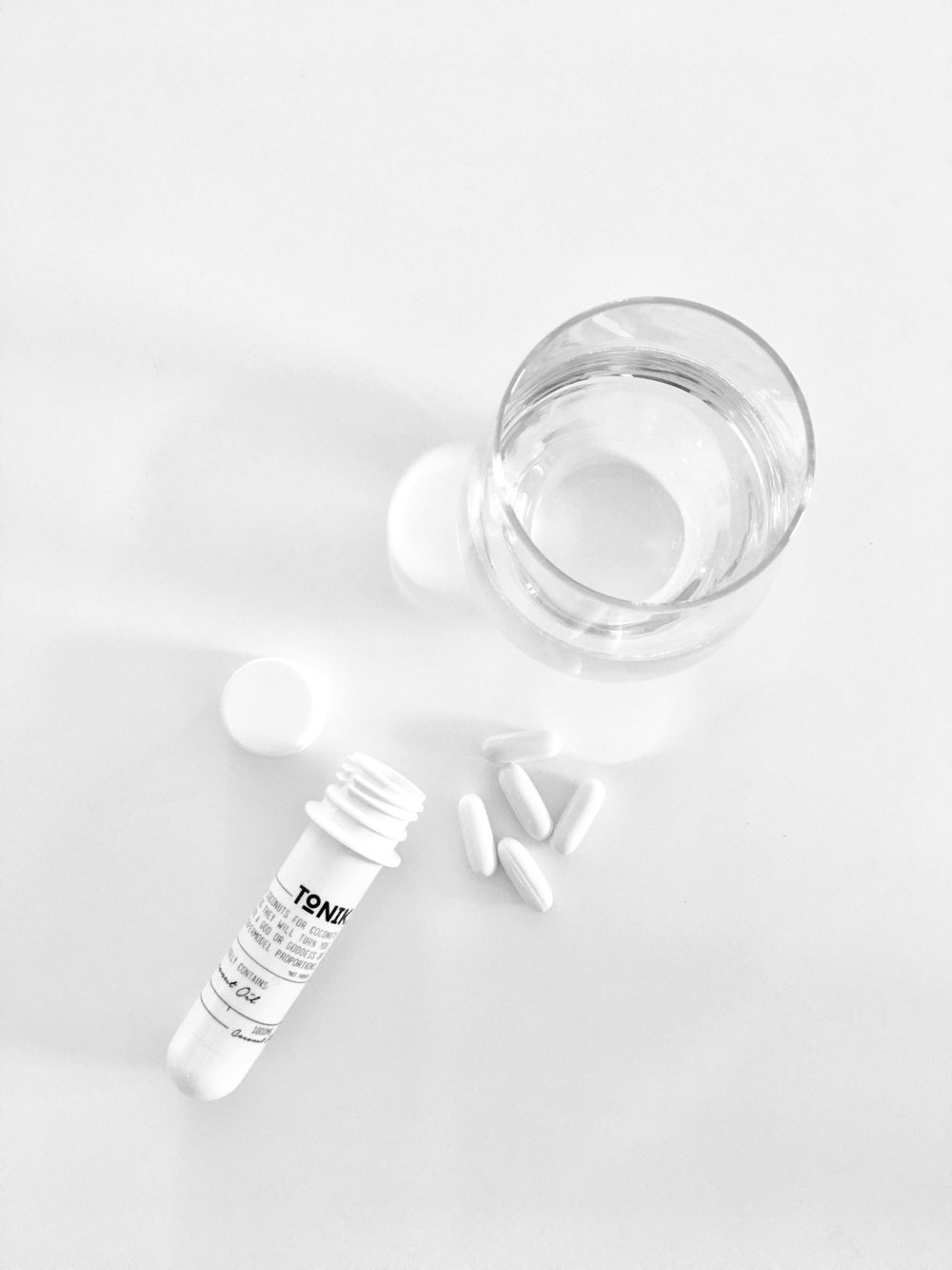 Geöffnete Dose mit weißen Kapseln neben einem Glas Wasser