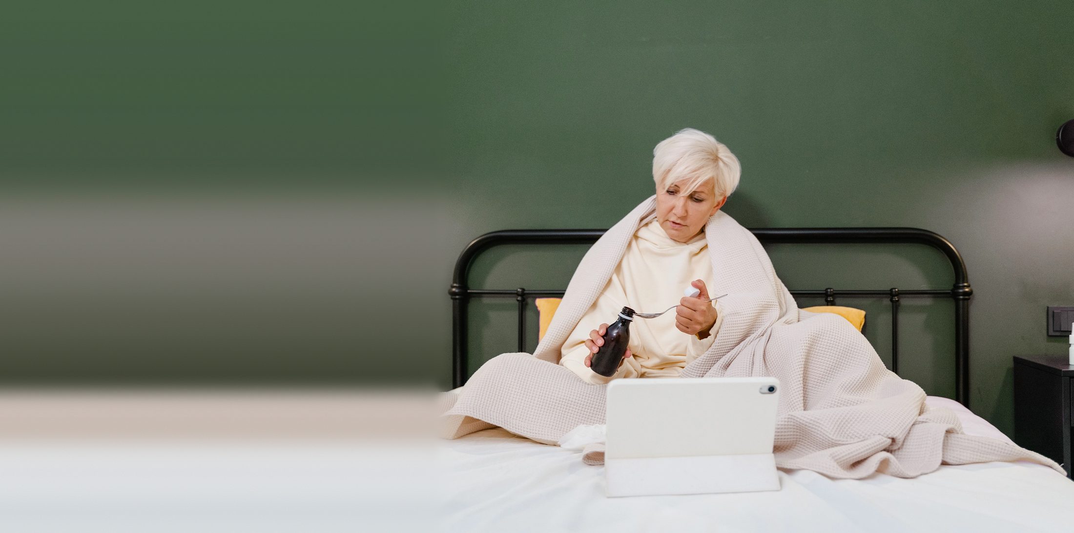 Frau im Bett mit Decke, Hustensaft und Tablet, Symbolbild für Beratung zu Arzneimitteln